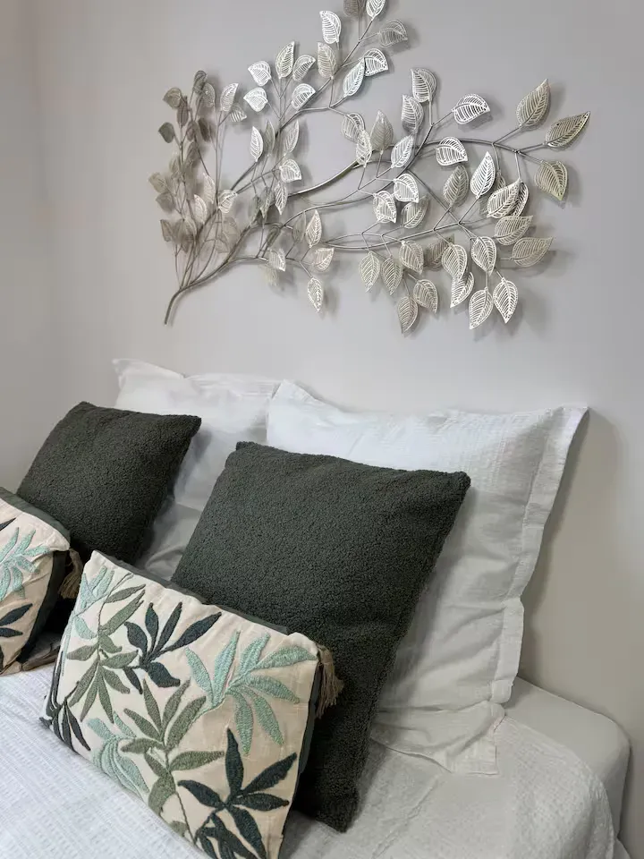 Chambre de La Suite Devosge à Dijon : tête de lit avec coussins verts et blancs et décoration murale en feuilles métalliques